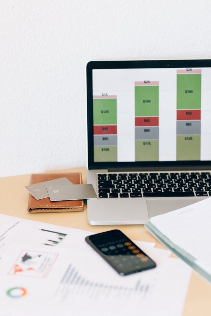 Laptop displaying financial chart alongside documents and credit cards on desk.