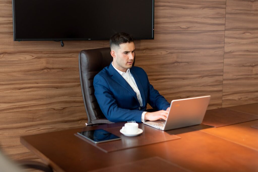 A focused businessman in a blue suit working on a laptop in a modern office setting.